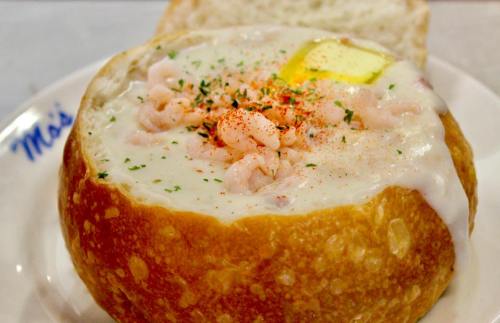 A bread bowl filled with creamy seafood chowder, topped with shrimp, butter, and a sprinkle of seasoning.