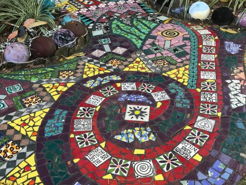 Colorful mosaic pathway with intricate patterns and designs, featuring various shapes and vibrant tiles.