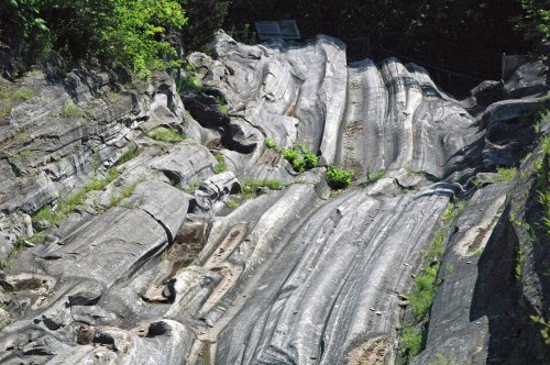 A rocky landscape with smooth, wavy stone formations and patches of greenery.