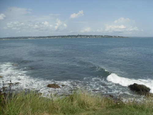 A serene coastal view with gentle waves lapping at rocky shores under a partly cloudy sky.