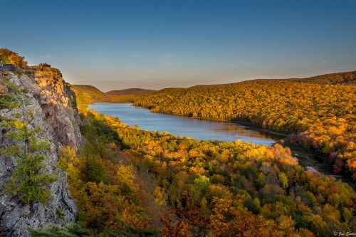 A scenic view of a river winding through vibrant autumn foliage and rocky cliffs under a clear blue sky.