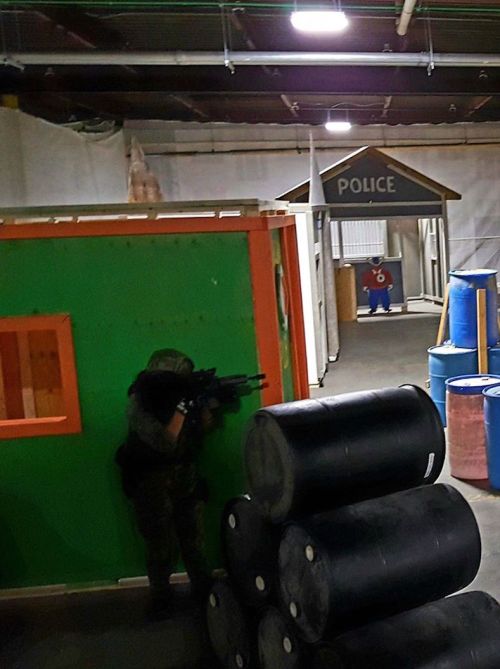 A soldier in tactical gear aims a weapon in a training facility with colorful structures and barrels.