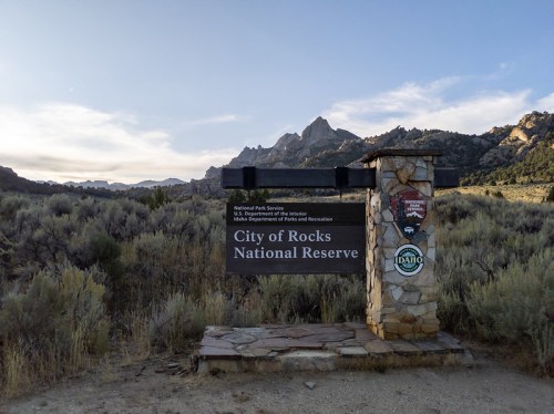 Sign for City of Rocks National Reserve, surrounded by sagebrush and mountains under a clear sky.
