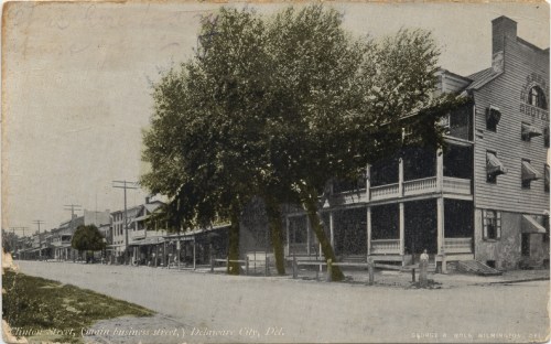 Historic black-and-white postcard of a Delaware City street, featuring trees and early 20th-century buildings.