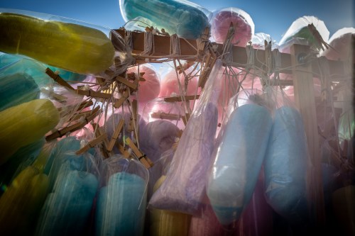 Colorful cotton candy in clear bags hanging on a wooden display against a bright blue sky.