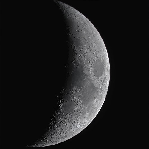 A close-up view of a crescent moon, showcasing its craters and surface details against a black background.
