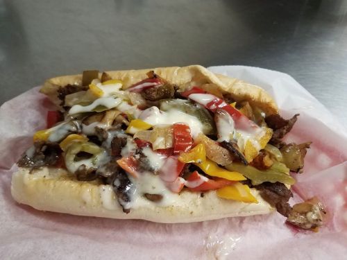 A loaded sandwich with grilled steak, colorful peppers, and melted cheese on a soft hoagie roll.