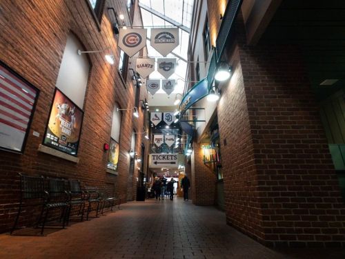 A brick hallway with hanging team banners and ticket signs, leading to a crowd of people in the distance.