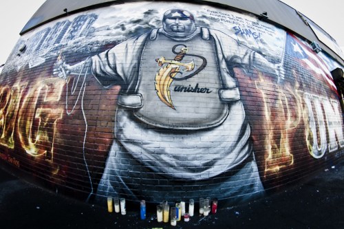 A large mural of a figure in a white outfit with a banana, surrounded by colorful graffiti and candles at the base.