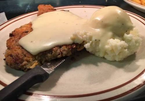 A plate featuring a breaded chicken cutlet topped with creamy gravy, served with a side of mashed potatoes.