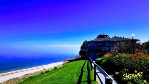 A scenic view of a coastal house overlooking the ocean, with vibrant greenery and a clear blue sky.