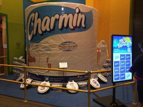 A large, playful display of Charmin toilet paper rolls in a colorful setting, with interactive screens nearby.