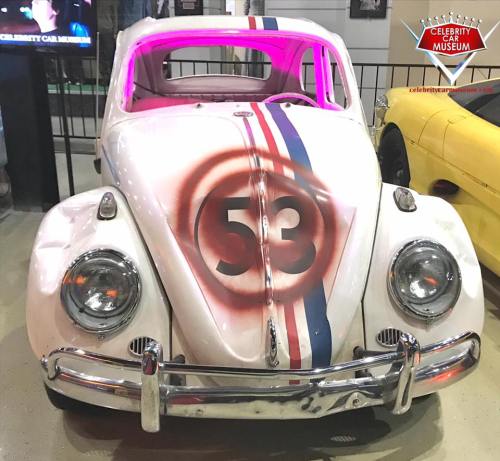 A vintage white Volkswagen Beetle with the number 53 and colorful stripes, displayed in a car museum.