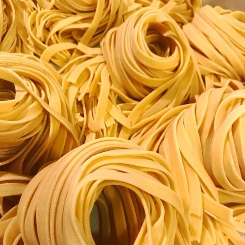 A close-up of freshly made yellow fettuccine pasta, arranged in loose, spiraled nests.