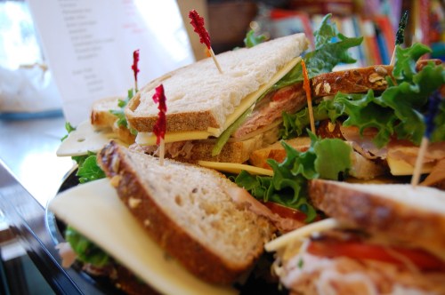 A close-up of a platter of sandwiches with layers of meat, cheese, and lettuce, garnished with decorative toothpicks.