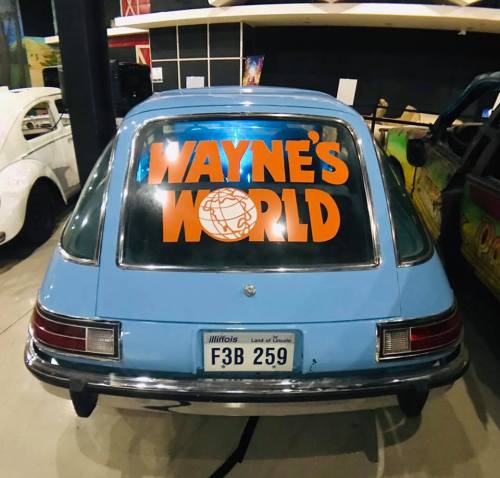 A blue car with a "Wayne's World" sticker on the back window, displayed in a museum or exhibit.