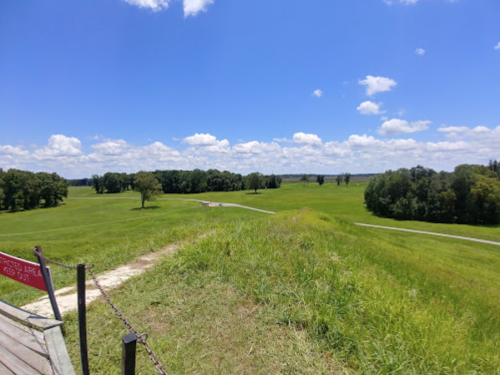 A panoramic view of a lush green landscape under a bright blue sky with scattered clouds.