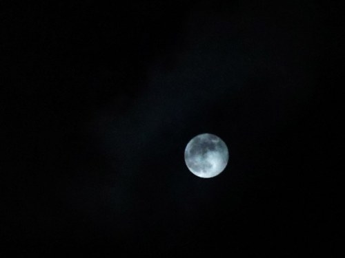 A bright moon partially obscured by dark clouds in a night sky.