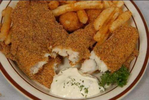 A plate of crispy fried fish fillets with fries, hushpuppies, and a side of tartar sauce garnished with parsley.