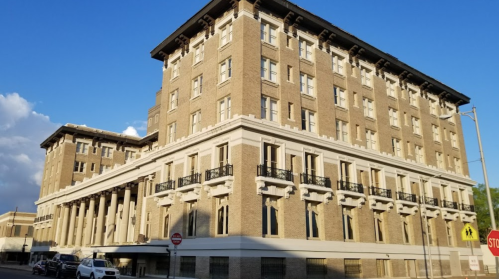 Historic brick building with multiple stories, large windows, and a decorative facade under a blue sky.
