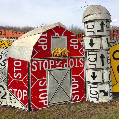 A whimsical barn and silo made from colorful traffic signs, featuring red stop signs and yellow accents.