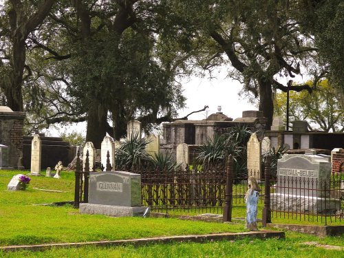 A serene cemetery scene with gravestones, lush greenery, and large trees in the background.