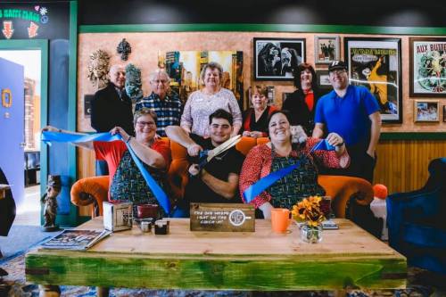 A group of people poses together in a cozy room, celebrating with blue ribbons and smiles.