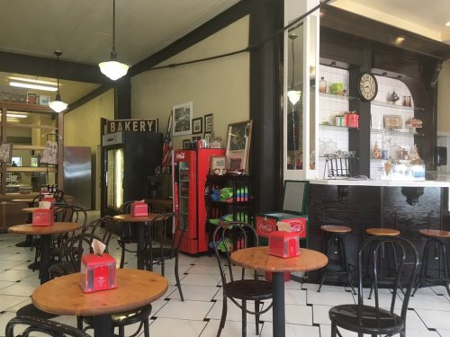Cozy bakery interior with wooden tables, black chairs, a vintage Coca-Cola machine, and decorative wall items.