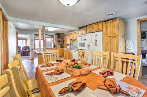 A spacious kitchen with wooden cabinets, a dining table set with an orange tablecloth, and a cozy living area in the background.