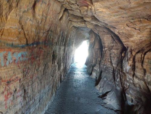 A narrow cave tunnel with rocky walls, leading to a bright light at the end.