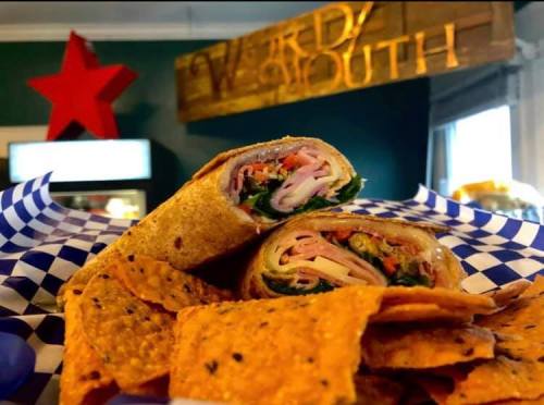 A close-up of a wrap filled with meats and vegetables, served with a side of tortilla chips on a blue checkered plate.
