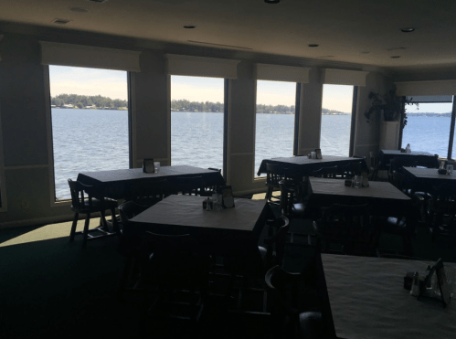 Interior of a restaurant with empty tables and large windows overlooking a lake. Natural light fills the space.