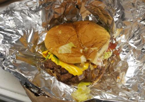 A partially eaten cheeseburger with lettuce, tomato, and onion, wrapped in foil.