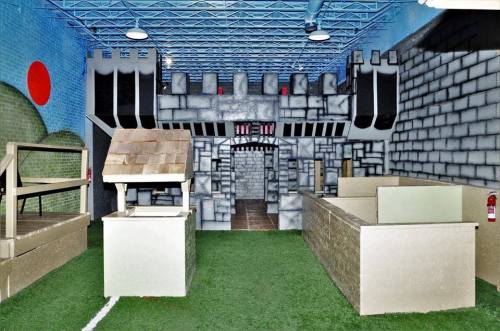 Indoor play area featuring a castle structure, playhouses, and green turf flooring. Brightly colored walls enhance the scene.
