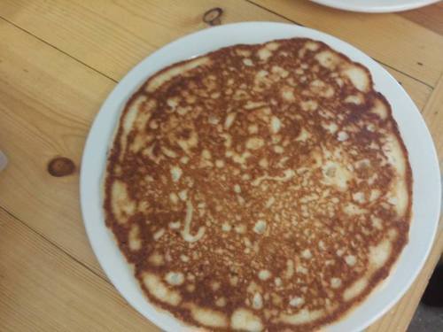 A golden-brown pancake on a white plate, resting on a wooden table.