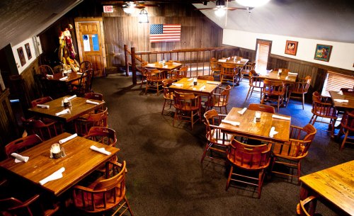 A cozy restaurant interior with wooden tables and chairs, featuring an American flag on the wall.