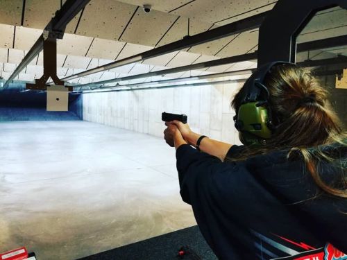 A person wearing ear protection aims a handgun at a target in a shooting range.