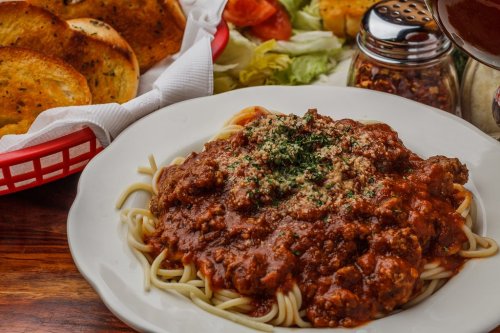 A plate of spaghetti topped with meat sauce and herbs, served with garlic bread and a side salad.