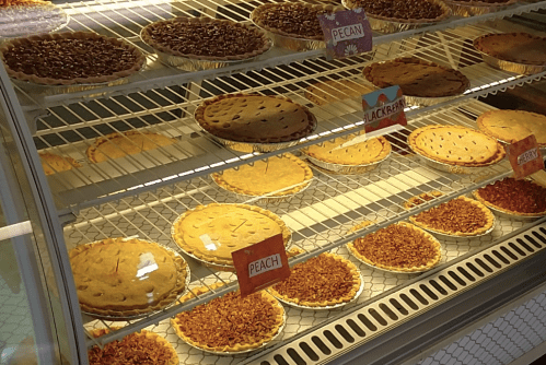 A display case filled with various pies, including pecan, peach, and blackberry, arranged on shelves.