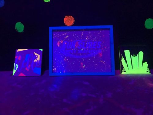 Three colorful, glowing signs under black light, featuring "FUNSLIDES" and abstract designs, against a dark background.