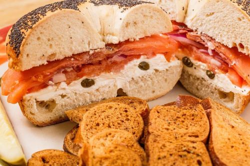 A sliced bagel filled with cream cheese, smoked salmon, tomatoes, and onions, served with toasted bread slices.