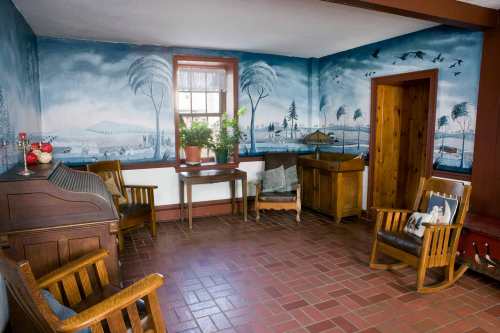Cozy room with wooden rocking chairs, a table, and a mural of a serene landscape on the walls.