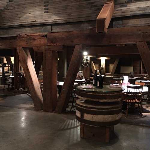 Interior of a rustic restaurant featuring wooden beams, tables, and a wine display on a barrel. Warm, inviting atmosphere.