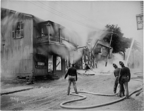 Firefighters battle a blaze in a historic building, with smoke and debris visible in a black-and-white photo.
