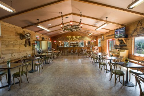 Interior of the Greenhorn Saloon featuring wooden decor, tables, and a bar area with a TV and rustic lighting.