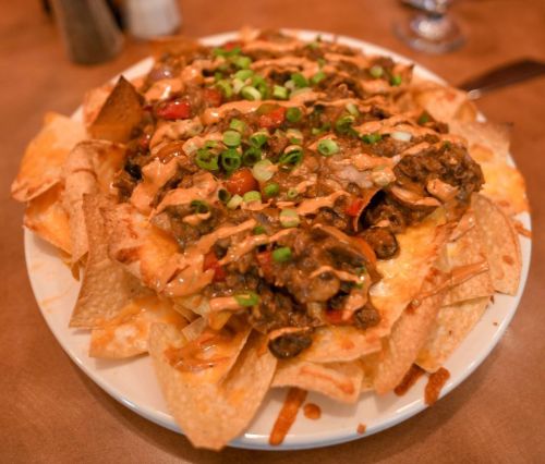 A plate of nachos topped with cheese, beef, diced tomatoes, and green onions, served on a wooden table.