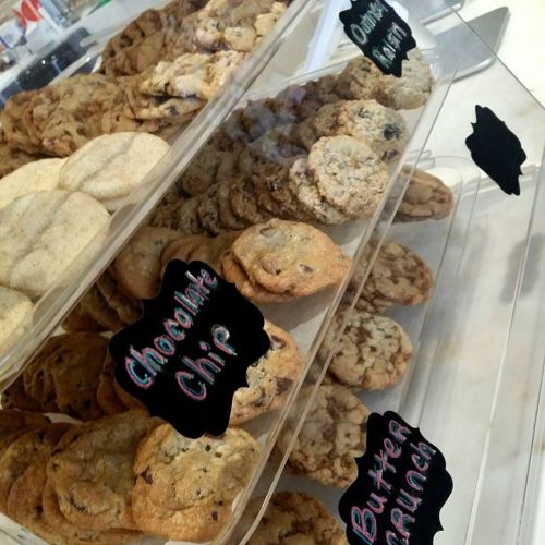 A display of assorted cookies, including chocolate chip, oatmeal, and butter crunch, in clear containers with labels.