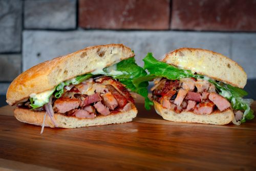 A freshly cut sandwich filled with layers of meat, lettuce, and mayonnaise, served on a toasted bun.