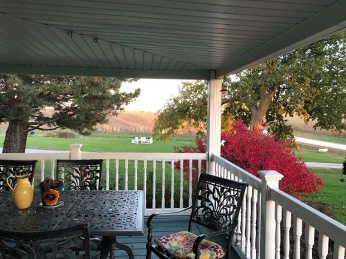 A cozy porch view with a table, chairs, and vibrant autumn foliage in the background.