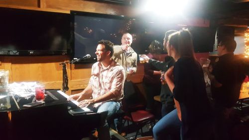 A lively bar scene with a pianist performing, surrounded by cheerful patrons enjoying drinks and singing along.
